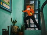 Person in orange shirt and red cap peeking through window.
