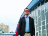 Man in superhero costume standing outside modern building.