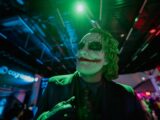 The joker smiles in the green and blue light.