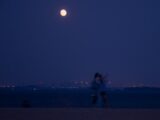 two people standing on a beach under a full moon