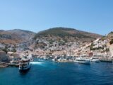 A vibrant view of Hydra Island's picturesque harbor with boats and buildings under a clear blue sky.