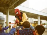 a man in a spider man costume is handing something to a child