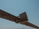 A metal padlock secures a rusty bar against sky.