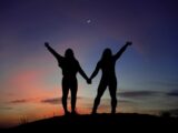 silhouette of 2 women standing on ground during sunset