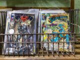 a metal basket filled with comic books on top of a table