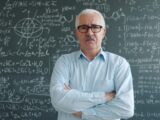 Professor with arms crossed in front of blackboard