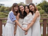 four women wearing dresses hugging