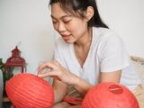 A young woman delicately assembling vibrant red paper lanterns indoors, capturing cultural tradition.