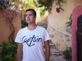 man in white crew neck t-shirt standing near brown wall during daytime