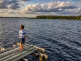boy in white t-shirt standing on wooden dock during daytime