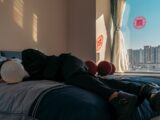a man laying on top of a bed next to a window