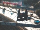 a batman mask on a fence near a highway