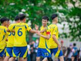 Youth soccer team wearing yellow jerseys celebrates during a match in Hanoi, Vietnam.